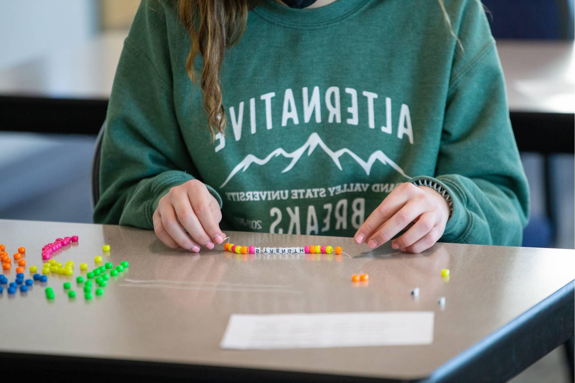 Student making a bracelet by putting beads onto a string